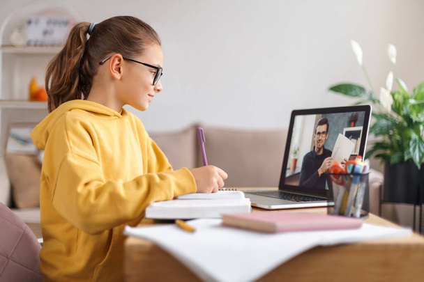 Koulutyttö ottaa videoneuvottelun online-opettaja kannettavan olohuoneessa kotona. Kotikoulu, etäopetus, sepelvaltimotautipandemian aiheuttama verkko-opetus. Sivunäkymä Verkko-oppimisen käsite - Valokuva, kuva