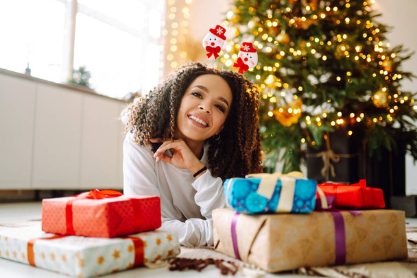 Happy lady with gifts near the Christmas tree. Young woman posing with presents in Christmas interior design. Fashion, celebration, holidays concept. - Fotó, kép