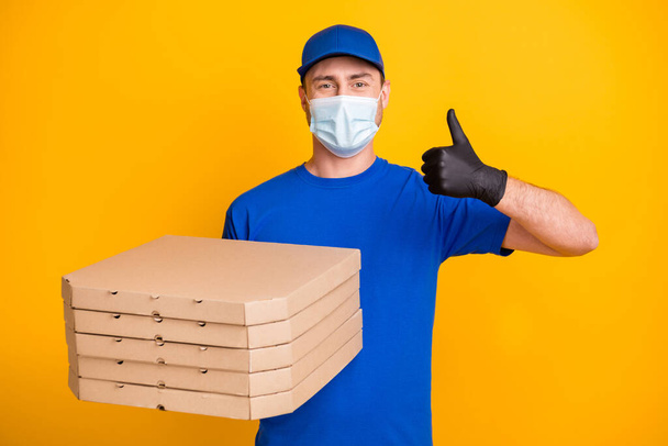 Photo of working guy headwear hold pizza boxes show thumb up safety respiratory isolated on yellow color background - Fotó, kép