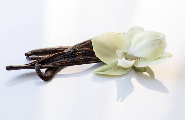 Сушеные ванильные стручки и цветы из орхидеи на белом фоне - Фото, изображение