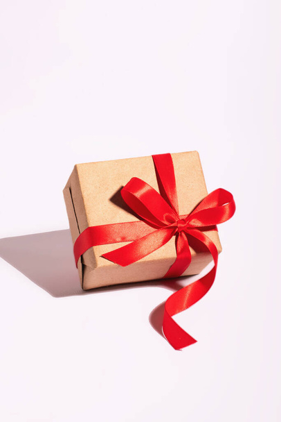 A gift in a kraft paper with red ribbon on a white background - Фото, изображение