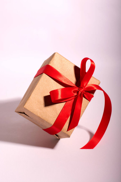 A gift in a kraft paper with red ribbon on a white background - Фото, изображение