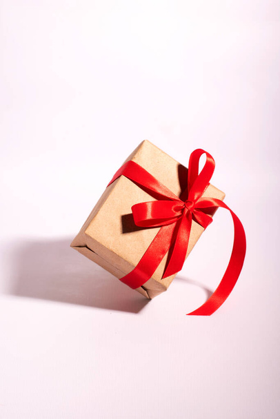 A gift in a kraft paper with red ribbon on a white background - 写真・画像