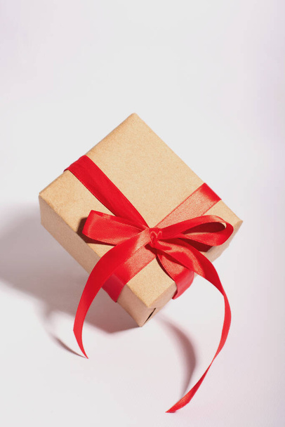 A gift in a kraft paper with red ribbon on a white background - Фото, зображення