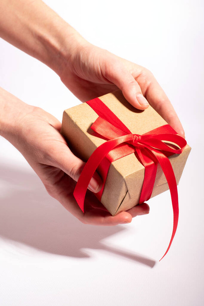 A gift with a red ribbon in woman's hands on a white background - Fotoğraf, Görsel