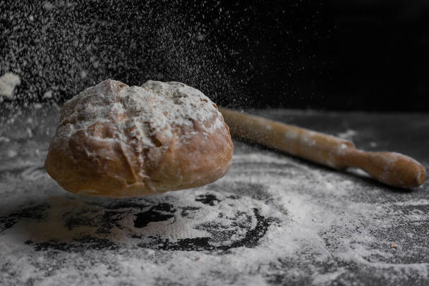 Bread flying with flour splash and rolling pin on floury black table.Concept of bakery, baking and cooking .Copy Space. - Foto, afbeelding