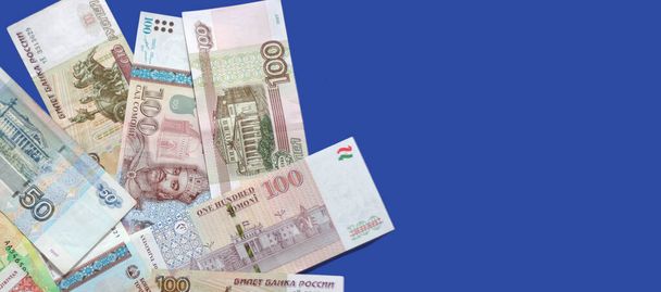 Photo de billets de banque somoni du Tadjikistan et de billets de banque en rouble russe sur fond bleu.  - Photo, image