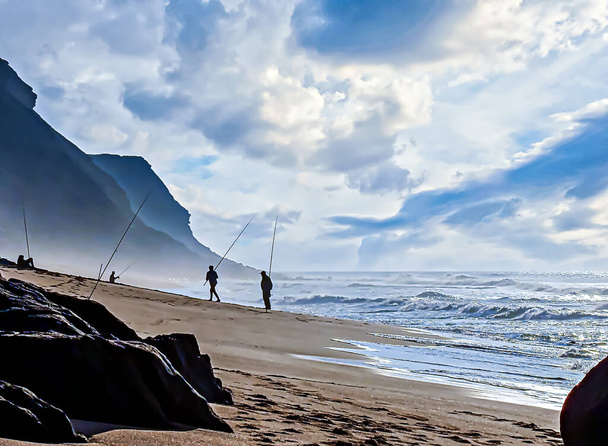 Lidé rybaří na pláži v mlhavé atmosféře při západu slunce - Fotografie, Obrázek