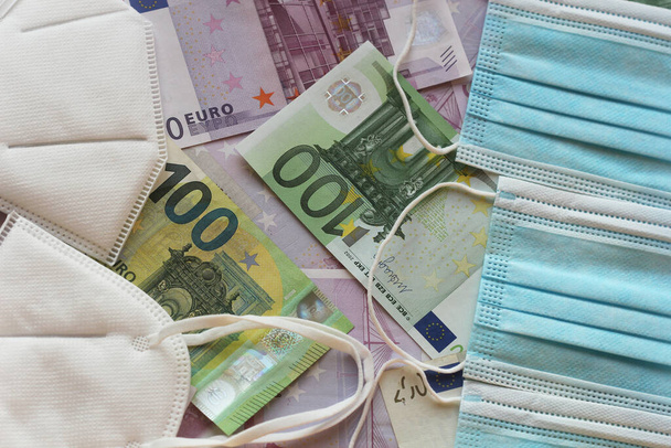 Tıbbi maske ve para. Cerrahi maske. COVID-19 yüz maskesi sıkıntısına neden oldu. Euro banknotları ve tıbbi yüz maskeleri. - Fotoğraf, Görsel