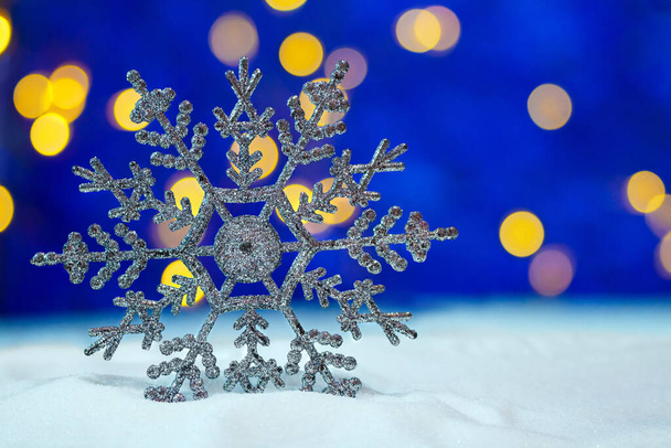 Grande fiocco di neve lucido nella neve e sfondo blu con bokeh giallo Buon Natale e biglietto di Capodanno. Copia spazio - Foto, immagini