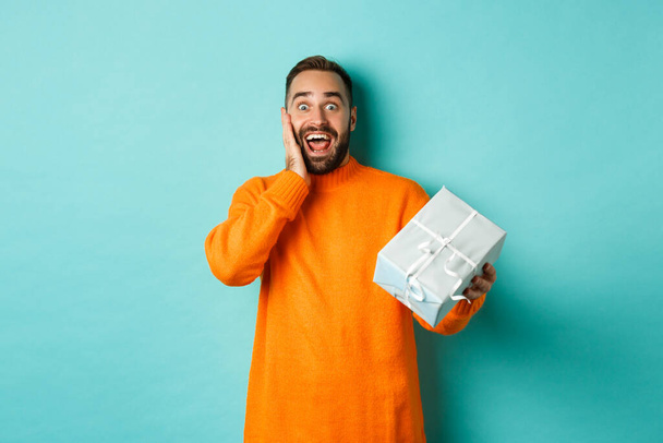Holidays and celebration concept. Surprised man receiving gift, looking happy at present and smiling, standing over blue background - Fotoğraf, Görsel