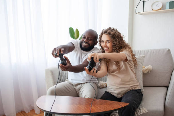 Happy weekend with a beautiful young family. Husband and pregnant wife sitting on the sofa in the living room are competing in video games. Relationships, family, video games and pregnancy concept. - Foto, afbeelding