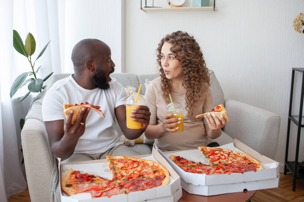 Monikansallisen parin uskomattomat tunteet urheilukilpailuja katsellessa. Raskaana oleva vaimo mehu ja pizza käsissään näyttää iloisesti miehelleen. Ihmiset, raskaus, ruoka ja urheilu käsite. - Valokuva, kuva
