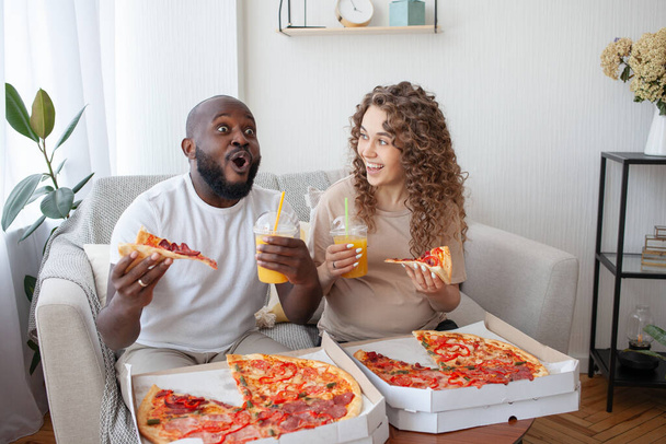 Emozioni incredibili di un uomo afroamericano mentre guarda una partita di calcio e mangia pizza con la sua moglie incinta carina. Concetto famiglia, riposo, cibo e gravidanza. - Foto, immagini