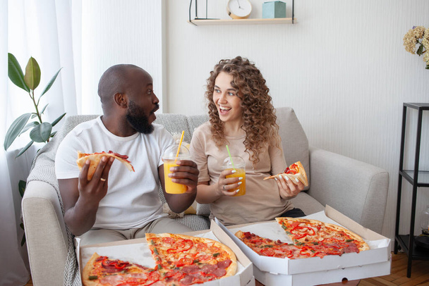Σγουρή έγκυος κοπέλα με τον άντρα της, που χρησιμοποιεί την παράδοση φαγητού, τρώει πίτσα και κοιτάζει ο ένας στα μάτια του άλλου συναρπαστικά. Εγκυμοσύνη, διατροφή και άνθρωποι έννοια. - Φωτογραφία, εικόνα