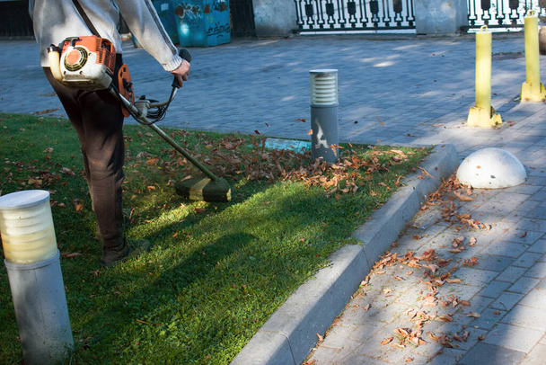 Φθινοπωρινή δουλειά στο πάρκο. Ο κηπουρός κόβει το γρασίδι πριν το χειμώνα.. - Φωτογραφία, εικόνα