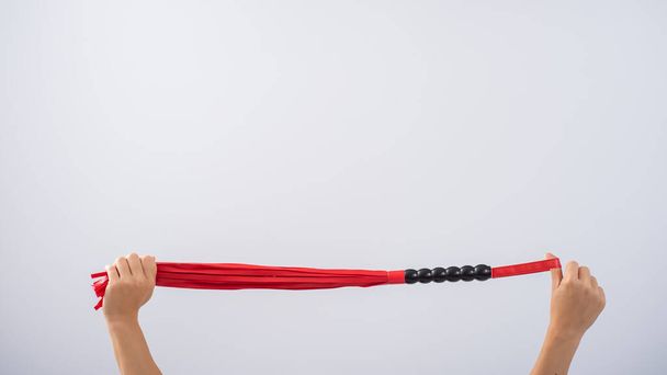 Red leather whip in female hands on a white background. Copy space. - Фото, изображение