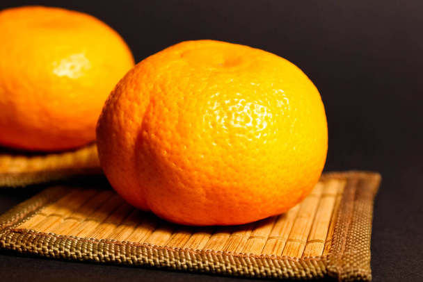 Een hele rijpe mandarijn op tafel op een zwarte achtergrond. Close-up, selectief schot. - Foto, afbeelding