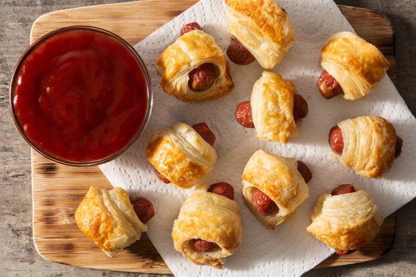 Pigs in blankets. Mini sausages wrapped in puff pastry with ketchup sauce. - Фото, изображение