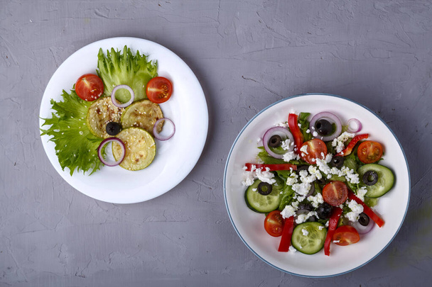 White plate with grilled zucchini with cherry tomatoes on lettuce leaves and greek salad on a concrete background. - Φωτογραφία, εικόνα