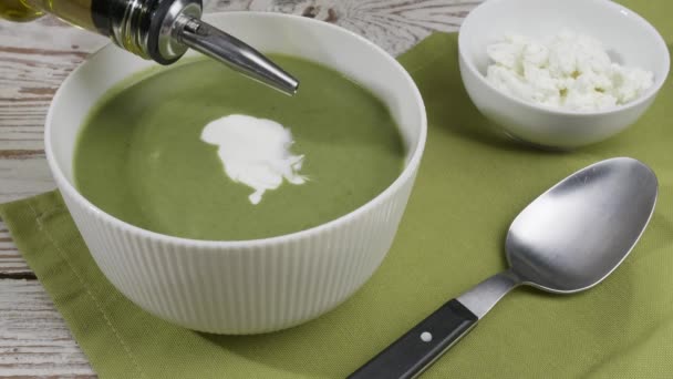 Woman dressing tasty spinach cream soup in bowl on table - Footage, Video