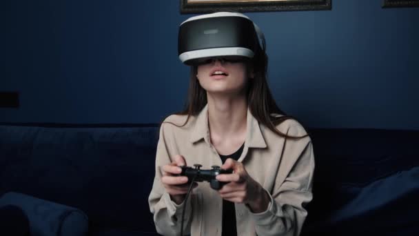 自宅でソファの上でエキサイティングな感情ビデオゲームをプレイする女性。ジョイスティックコントローラーとヘッドセットヘルメットコントロールゲームを使用しています。教育、技術、エンターテイメント、仮想現実の概念 - 映像、動画
