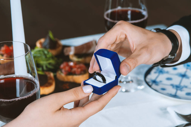 Ο άντρας δίνει σε μια γυναίκα ένα έξυπνο δαχτυλίδι πληρωμής. Ρομαντικό δείπνο. Ανδρικά χέρια με μπλε βελούδινο κουτί που περιέχει πληρωμές έξυπνο δαχτυλίδι. Ημέρα του Αγίου Βαλεντίνου - Φωτογραφία, εικόνα