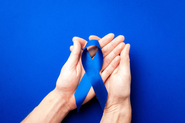 Блакитна стрічка простати. Оголошення про рак передміхурової залози у листопаді. Блакитна стрічка в руках ізольована на темно-синьому фоні. Листопад і міжнародний день чоловіків - Фото, зображення