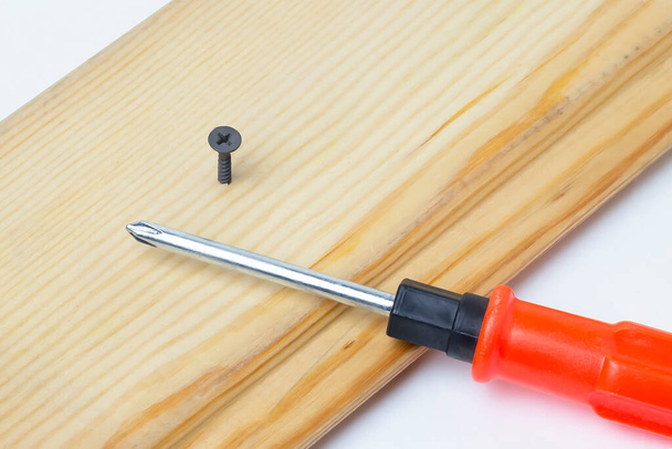 Screwdriver and screwed screw on a wooden board. On a white background. - Photo, Image