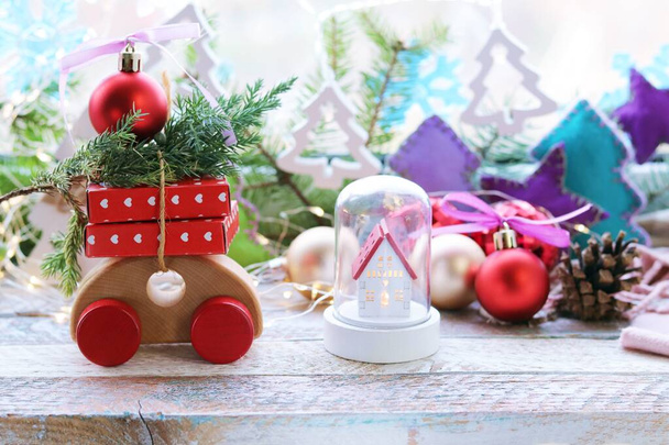 Новорічний іграшковий будинок, дерев'яний автомобіль з подарунками та деревом, новорічні прикраси, освітлення, гілки ялинки на фоні вікна, концепція домашнього затишку, привітання, листівка
  - Фото, зображення
