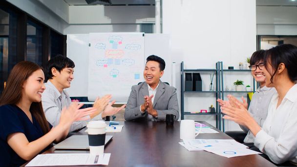 Group of happy Asian business people discuss together in team brainstorm meeting and clap hand, work late night in office. Corporate business, coworker teamwork, or project success celebration concept - Fotoğraf, Görsel
