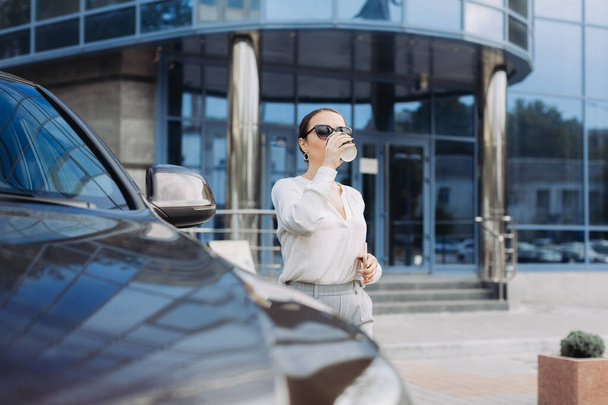 Geschäftsfrau trinkt Kaffee und checkt ihr Handy auf dem Weg zur Arbeit - Foto, Bild