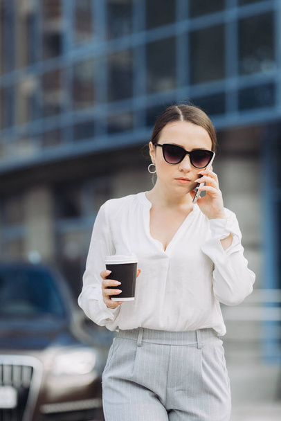 Деловая женщина, идущая по улице в деловом районе, разговаривает по телефону. - Фото, изображение