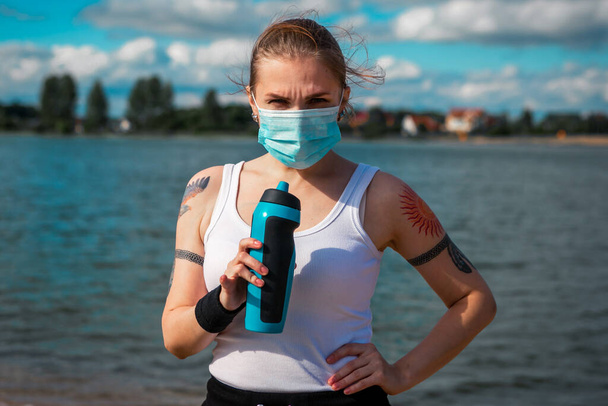 Mujer con máscara quirúrgica hacer entrenamiento en la playa, concepto coronavirus - Foto, imagen