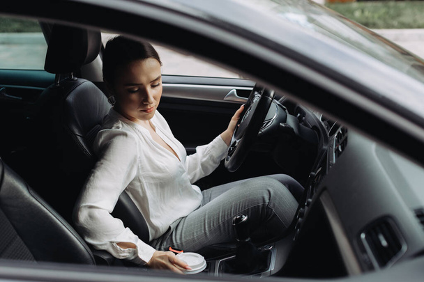 nainen juo kahvia ja tarkistaa puhelimensa autossa seisoo liikenneruuhkassa - Valokuva, kuva