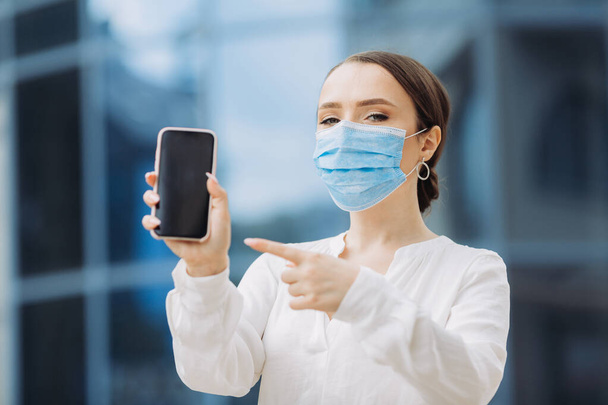 business woman in a protective mask holding a phone - Фото, изображение
