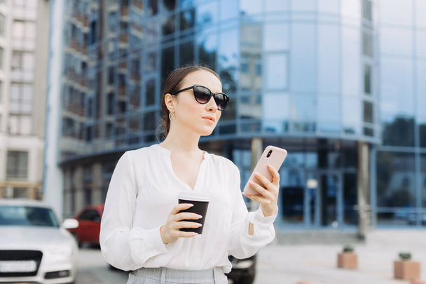 Donna d'affari che cammina per strada nel quartiere degli affari, controlla il suo smartphone. - Foto, immagini