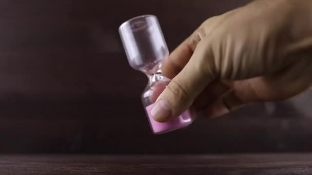 Ręka mężczyzny odwraca klepsydrę z różowym piaskiem - Materiał filmowy, wideo