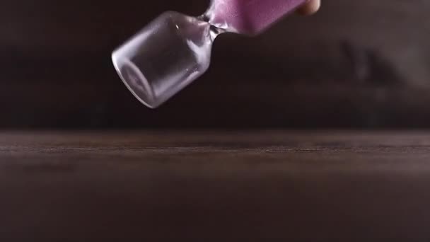Die Hand eines Mannes dreht sich um eine Sanduhr mit rosa Sand - Filmmaterial, Video