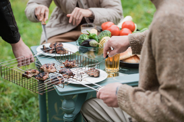 A young couple celebrates their wedding anniversary on a country plot. They roast meat, drink beer, relax in nature. - Foto, Bild