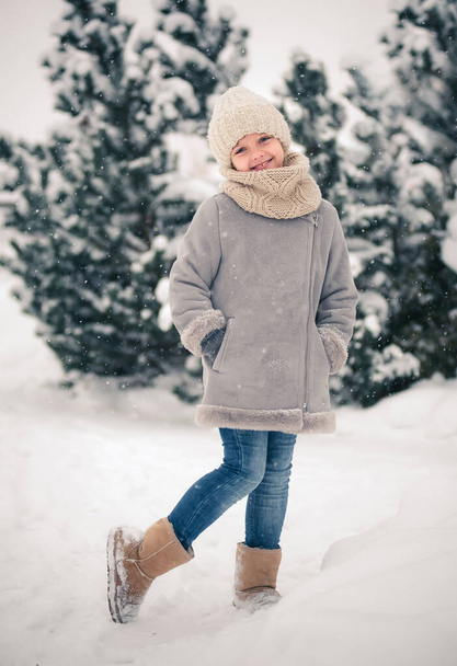 Красивая улыбающаяся маленькая девочка зимой в теплой одежде в снежном лесу. - Фото, изображение