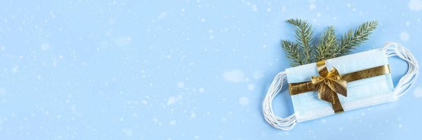 Medizinische Schutzmasken mit goldenem Band und Tannenzweig isoliert auf blauem Hintergrund. Ein Geschenk zu Weihnachten und Neujahr 2021. Coronavirus-Pandemiekonzept. Kopierraum. Banner. - Foto, Bild