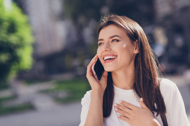 Photo portrait of laughing girl touching chest with hand talking on phone in park - Φωτογραφία, εικόνα