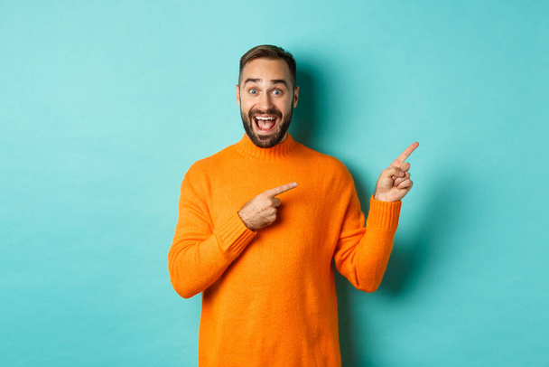 Excited man making an announcement, pointing fingers right your logo, standing over turquoise background - Foto, afbeelding