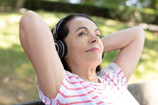 grandmother listens to music on headphones outdoors - Foto, afbeelding