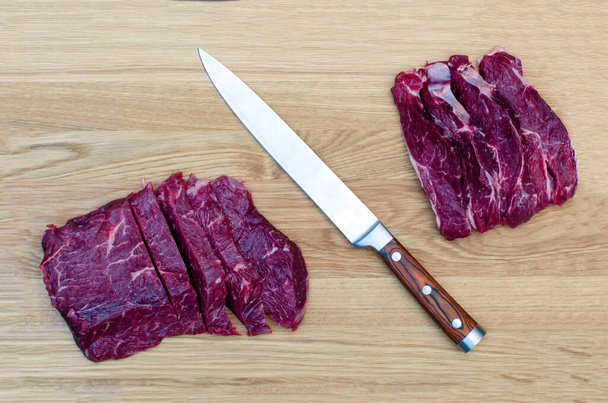 Rohes Fleisch in Scheiben geschnitten mit einem Küchenmesser auf einem Schneidebrett, schwarzer Teller mit Scheiben von geschnittenem Fleisch. - Foto, Bild