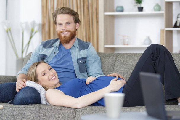 couple with pregnant woman relaxing on sofa together - Foto, afbeelding