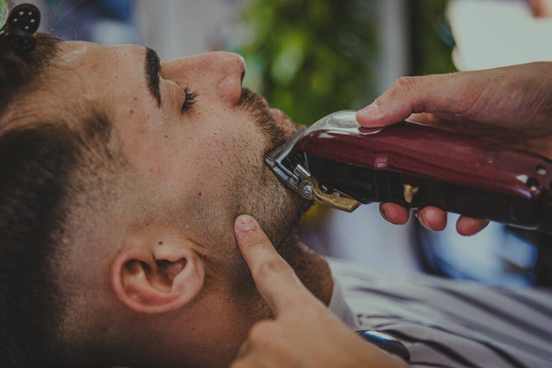 detalhe de um jovem com braços tatuados corta o cabelo de um homem em uma barbearia - Foto, Imagem