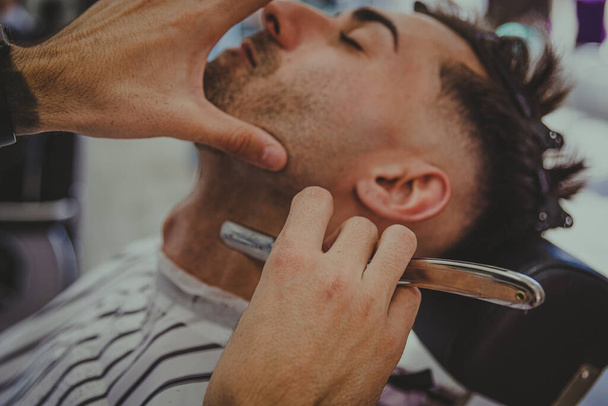 Dövmeli bir gencin ayrıntıları berber dükkanında bir adamın saçını kesiyor. - Fotoğraf, Görsel