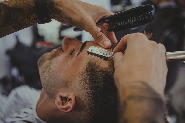 detail of a young man with tattooed arms cuts a man's hair in a barber shop - Fotoğraf, Görsel